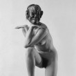 Corps-sculpture avec masque prenant pose à genoux avec bras repliés.